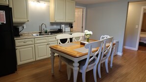 Una cocina con armarios blancos, una mesa de comedor de madera y sillas blancas.