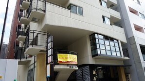 Un edificio de varios pisos con balcones, una tienda con un letrero y un coche estacionado.