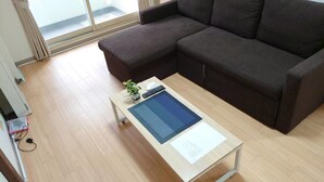 Una sala de estar moderna con un sofá marrón oscuro, una mesa de centro de madera con una tableta, una planta pequeña y un control remoto.
