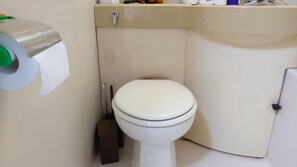 Un baño pequeño y funcional con inodoro blanco, dispensador de papel higiénico y un armario.