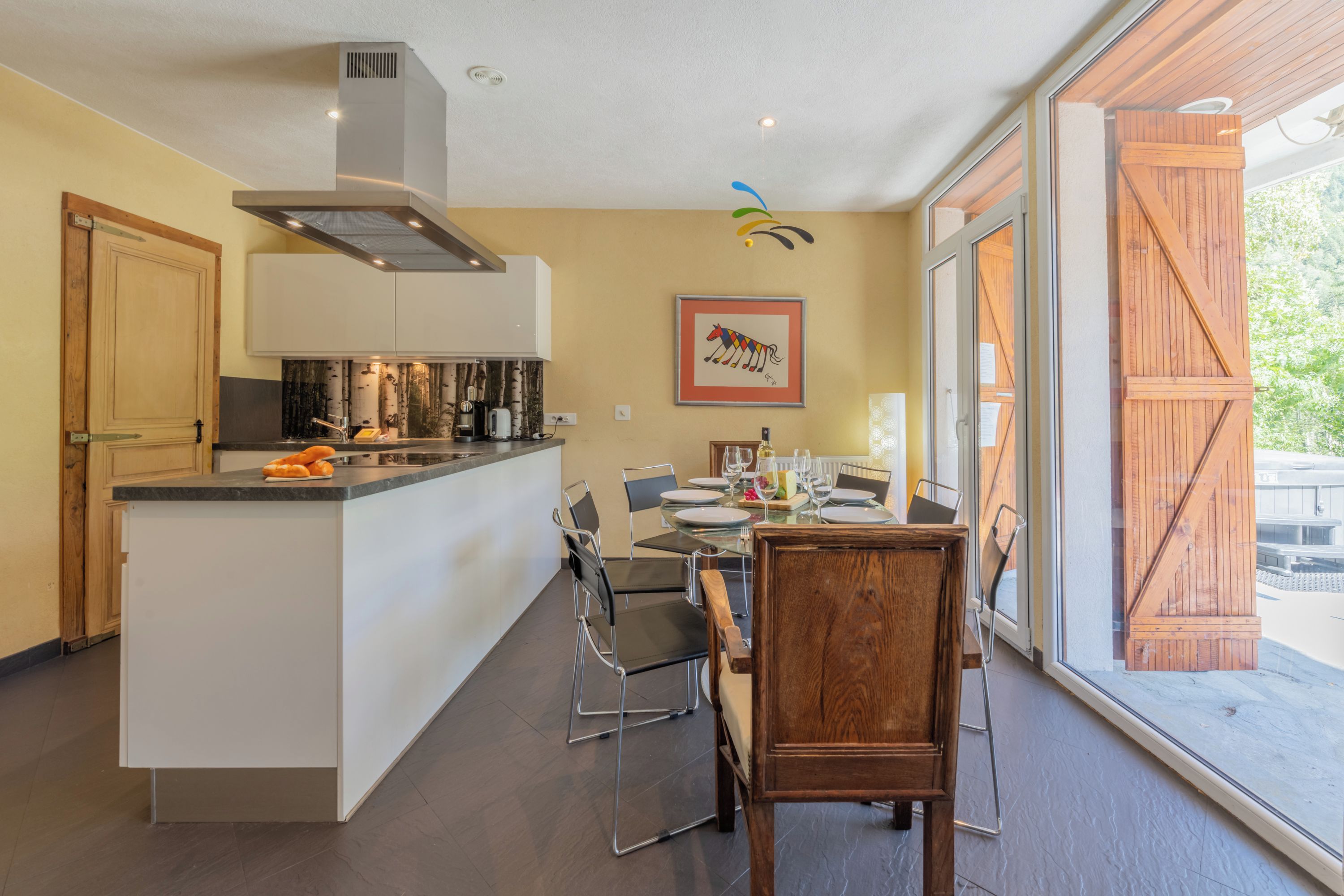 Een moderne keuken met een centraal eiland, een eethoek met stoelen en een groot raam met uitzicht.