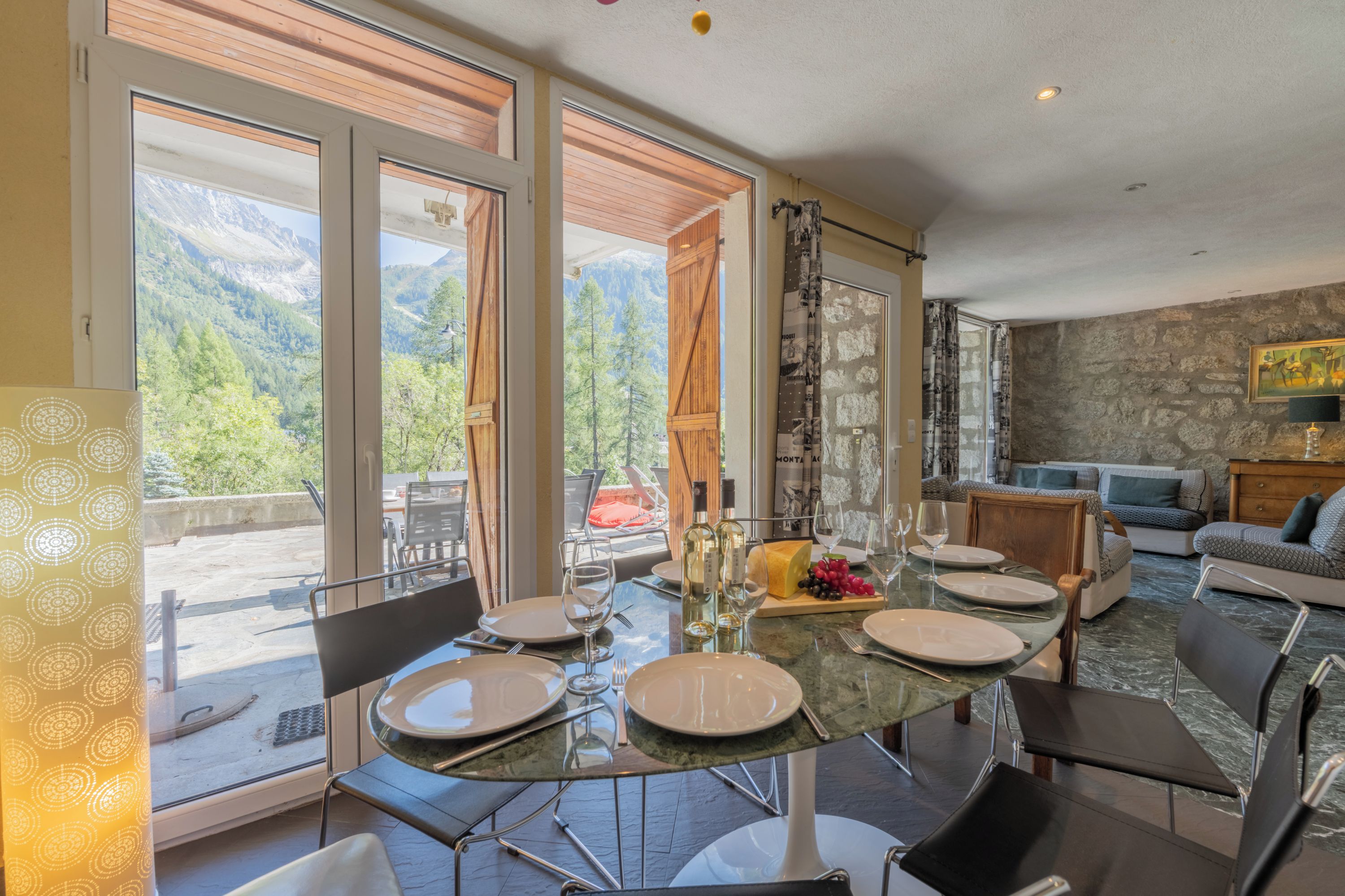 Un coin repas avec une table dressée pour six personnes, offrant une vue sur un paysage montagneux grâce à de grandes fenêtres.