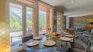 Un coin repas avec une table dressée pour six personnes, offrant une vue sur un paysage montagneux grâce à de grandes fenêtres.