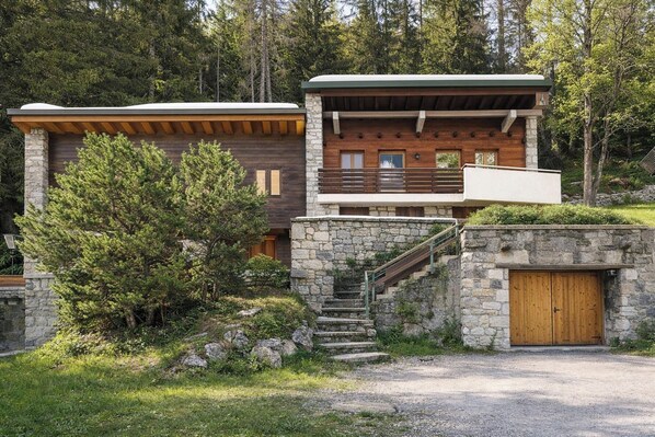 Een chalet met een stenen gevel, een houten terras en een trap naar een tweede verdieping.