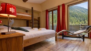 Ein Zimmer mit Etagenbett, Nachttisch mit Lampe, Stuhl am Fenster und Blick auf einen bewaldeten Berg.