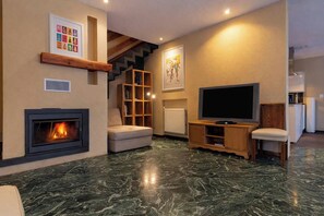 Una sala de estar con chimenea, televisor, sofá y una escalera.