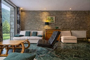 Una sala de estar con pared de piedra, un sofá, un sillón, una mesa y una lámpara.