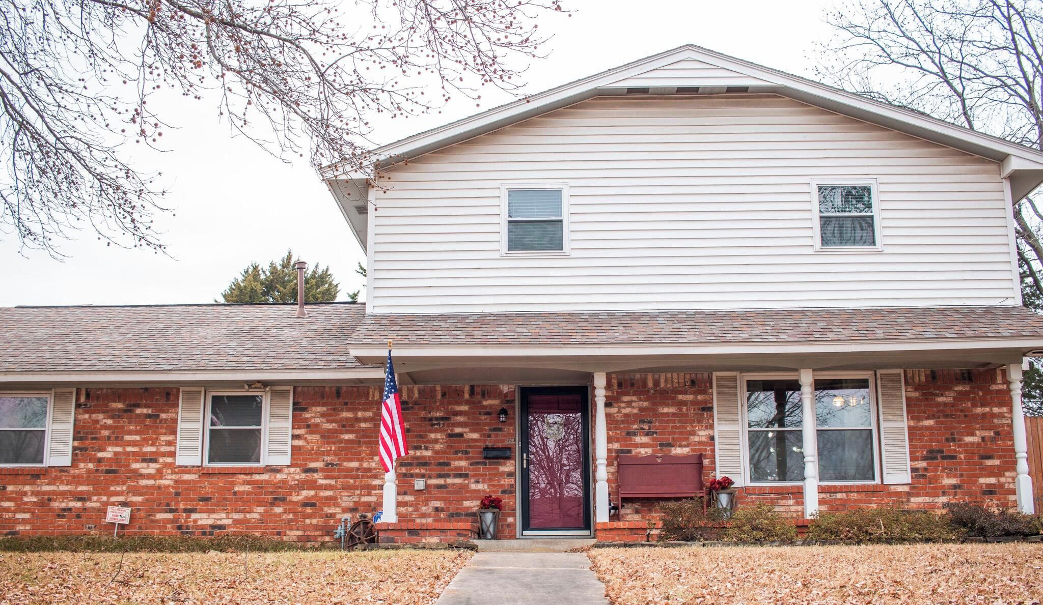 A two-story house with a brick facade, a front porch, and a red door.