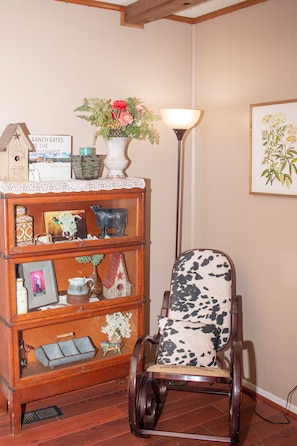 Une chaise en bois rustique avec un coussin à motifs de peau de vache, une bibliothèque en bois ornée de divers objets décoratifs et un lampadaire.