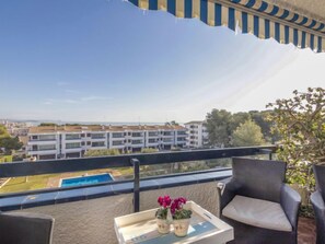A balcony with a view of a swimming pool, a chair, and a table with potted plants.
