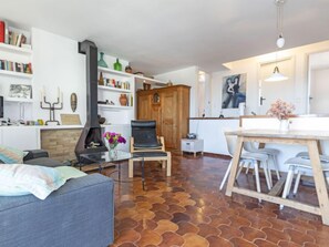 A living room with a fireplace, a dining area with a table and chairs, and a kitchen area with a wooden cabinet.