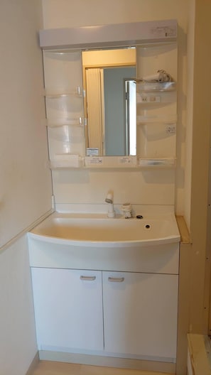 A white bathroom with a sink, mirror, and storage cabinets. - Hokusei Building 6F (Sapporo)