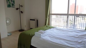 A hotel room with a bed, a standing fan, a heater, and a view of the outside. - Hokusei Building 6F (Sapporo)