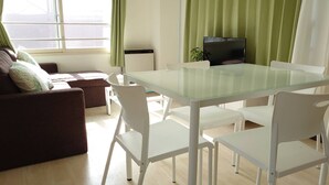 A modern living room with a glass-top dining table, white chairs, a brown sofa, and a television. - Hokusei Building 6F (Sapporo)