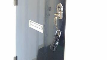 Puerta con un letrero de 'Welcome', un llavero, una alarma de emergencia roja y una cerradura electrónica.