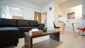 A modern living room with a dark grey sofa, a wooden coffee table with a tissue box, a small black chair, and a red chair. - IK Minami 6JO Residence 901 (Sapporo)