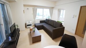A modern living room with a sectional sofa, a flat-screen TV, a coffee table, and a large window providing natural light. - IK Minami 6JO Residence 901 (Sapporo)