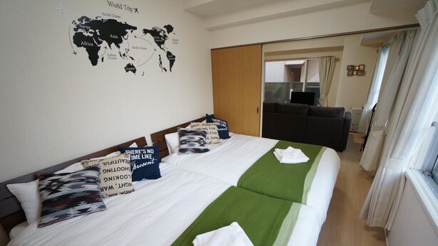 A hotel room with two beds, a world map on the wall, a green bedspread, and a view of the living area. - IK Minami 6JO Residence 901 (Sapporo)