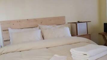 Un lit bien fait, avec du linge de lit et des serviettes blancs, une tête de lit en bois et un tableau encadré au mur.
