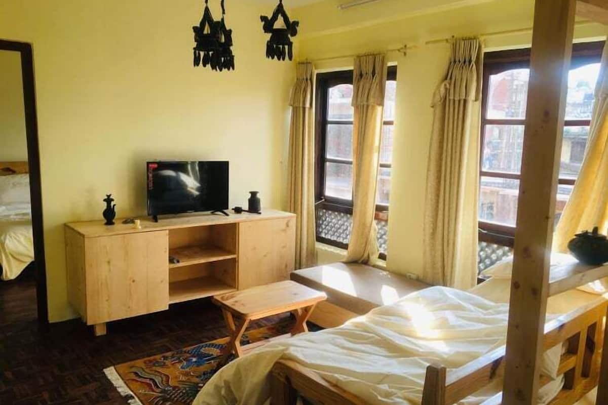 A room with a bed, a wooden TV stand, a small table, and a window with curtains.