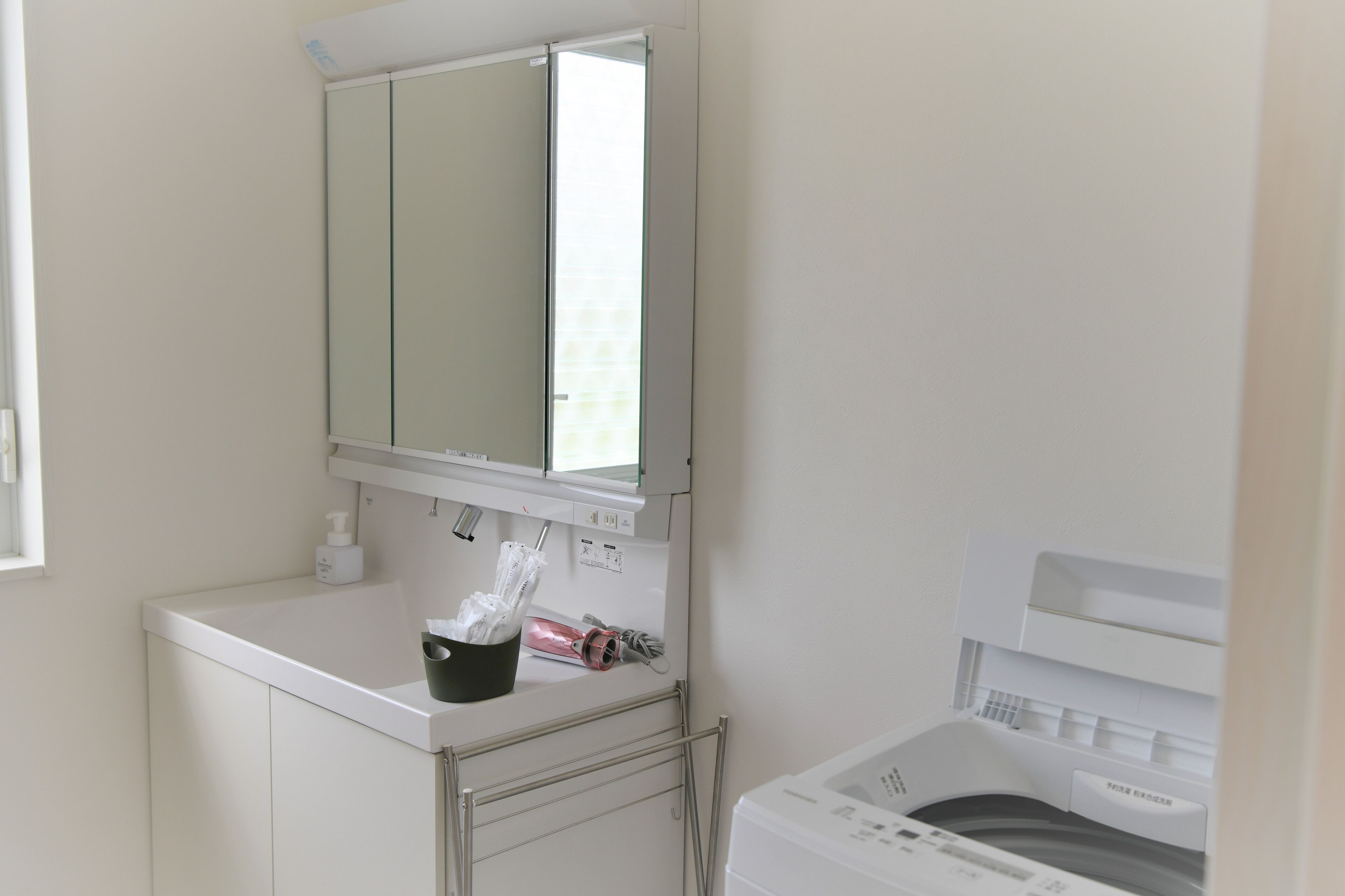 A clean, modern bathroom with a white sink, a mirror, and a washing machine.