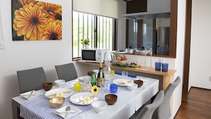 A dining area with a table set for four, a microwave, a fruit bowl, and a window with blinds. - Miyakojima White House Annex (Miyakojima)