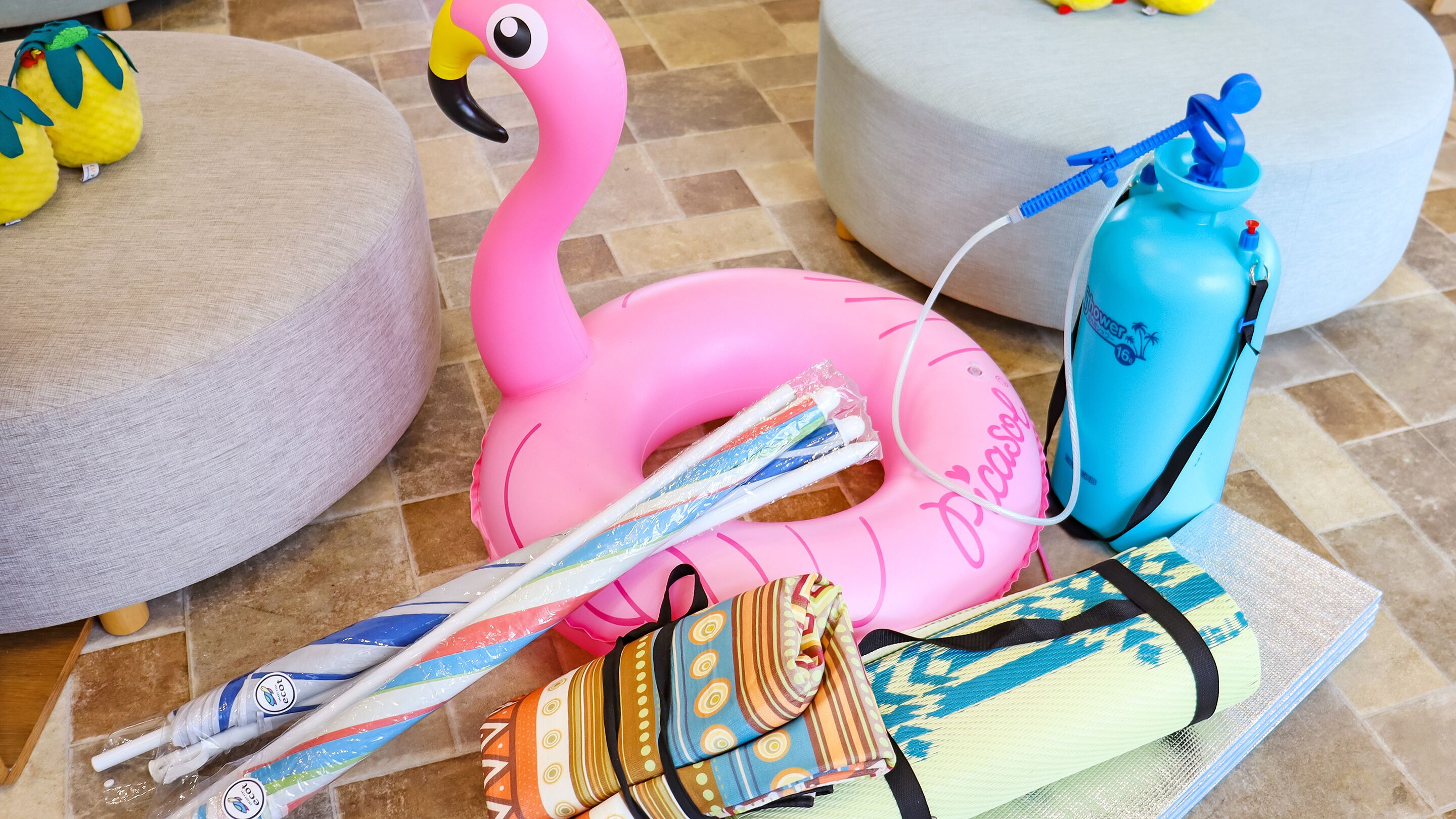 En uppblåsbar, rosa flamingo, en blå vattenflaska och en randig väska på ett kaklat golv.