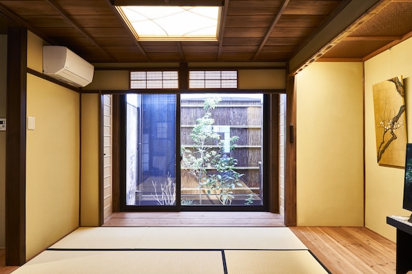 A traditional Japanese room with tatami flooring, a sliding door leading to a garden, and a ceiling fan.