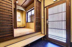A traditional Japanese room with tatami flooring, a wooden bench, sliding doors, and a view through a window.