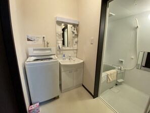 A modern bathroom with a washing machine, sink, and glass shower enclosure.