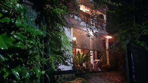 Un edificio con un espacio exterior techado, plantas en macetas y un sendero que lleva a la entrada.