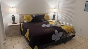 A bedroom with a bed, nightstands, lamps, a window with blinds, and a door. - Holiday Hideout by Paradise Resort Vacations (Clermont)