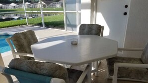 A patio area with a white table and chairs, a glass of water, and a view of a swimming pool and greenhouses in the background. - Holiday Hideout by Paradise Resort Vacations (Clermont)