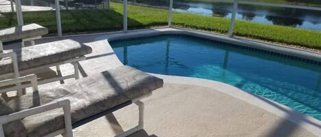 A swimming pool with stone steps and a view of a lake and houses in the background.