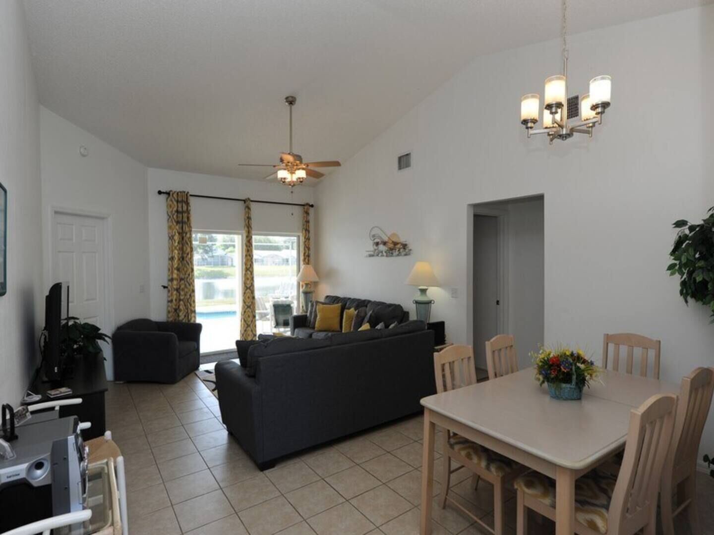 A living room with a sofa, a dining table with chairs, a ceiling fan, and a chandelier.