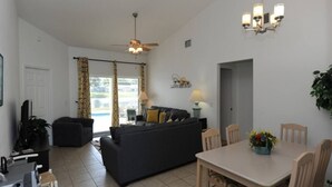 A living room with a sofa, a dining table with chairs, a ceiling fan, and a chandelier. - Holiday Hideout by Paradise Resort Vacations (Clermont)