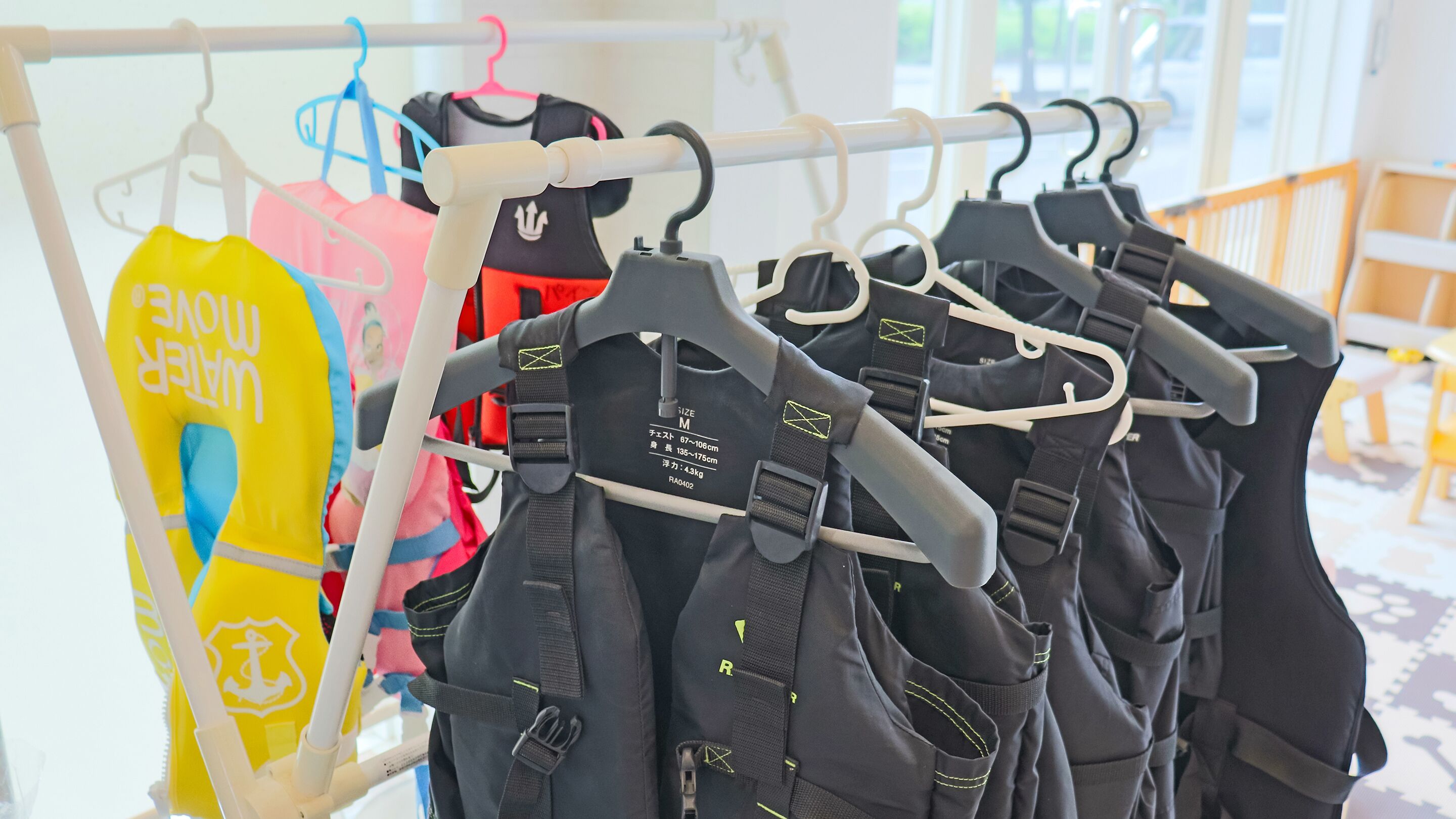 A rack of life jackets and wetsuits hanging on a wall.