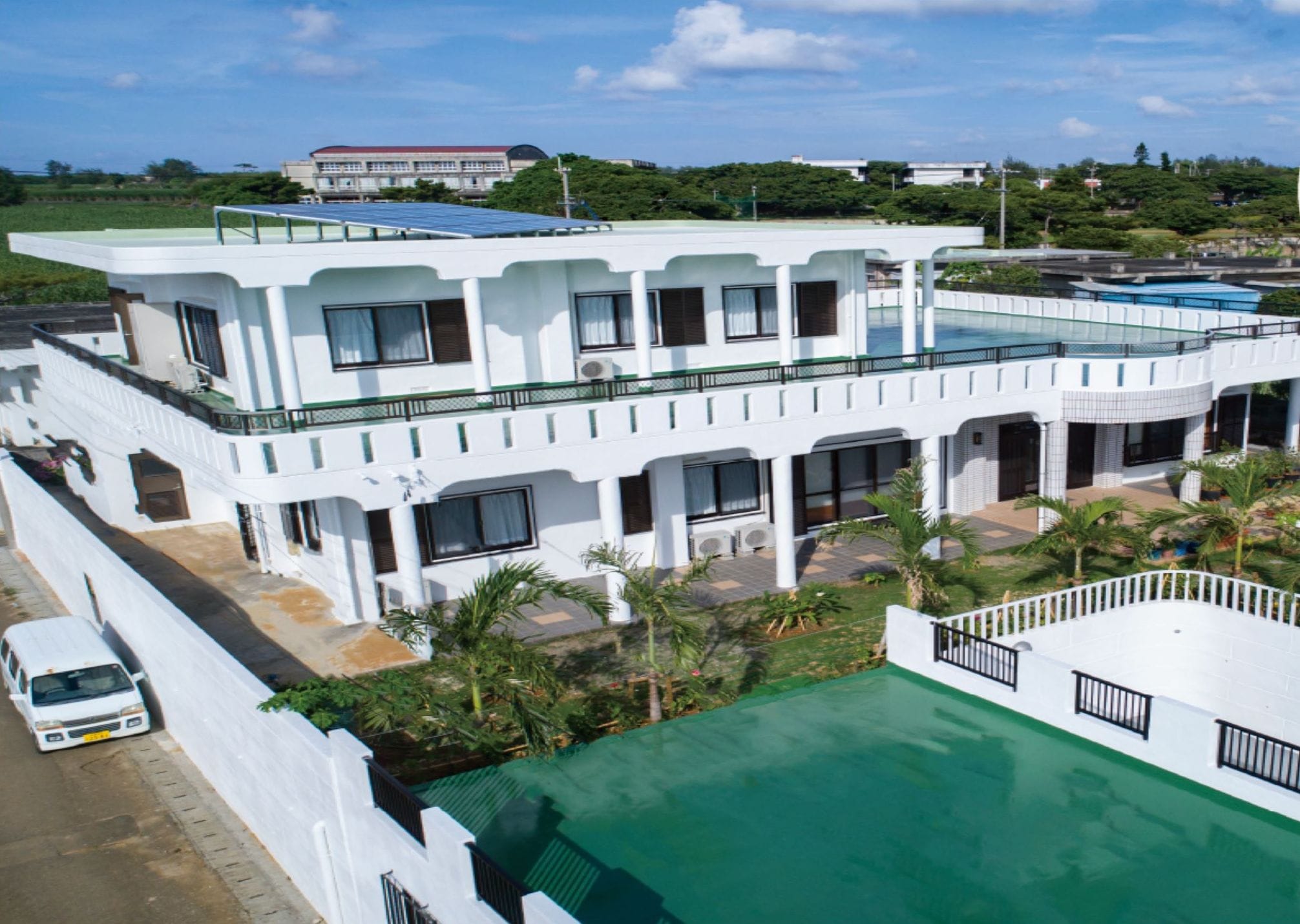 A modern white house with a large green pool and a covered patio area.
