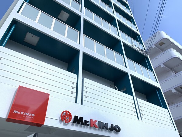 Un immeuble à plusieurs étages, sur lequel on peut voir une grande enseigne « M. Kinjo » au niveau inférieur.