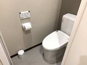 Une petite salle de bain propre, équipée de toilettes, d’une poubelle et d’un distributeur d’essuie-tout.