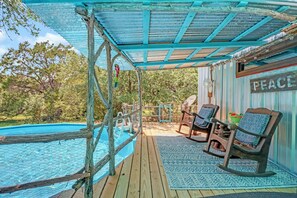 Une terrasse en bois avec une piscine, des fauteuils à bascule en bois et un panneau sur lequel on peut lire « PAIX ».