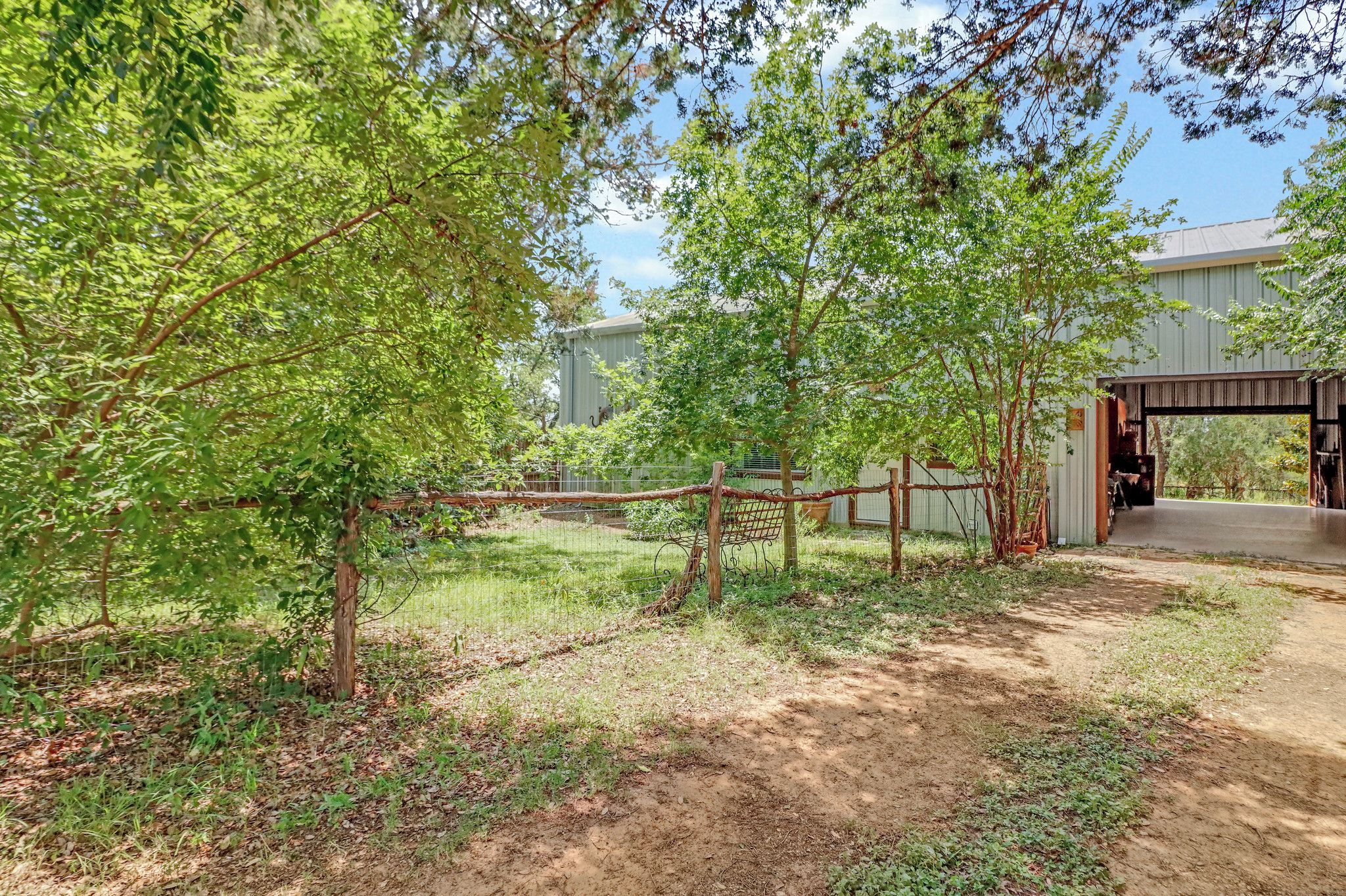 A fenced outdoor area with trees, a building entrance, and a dirt path.