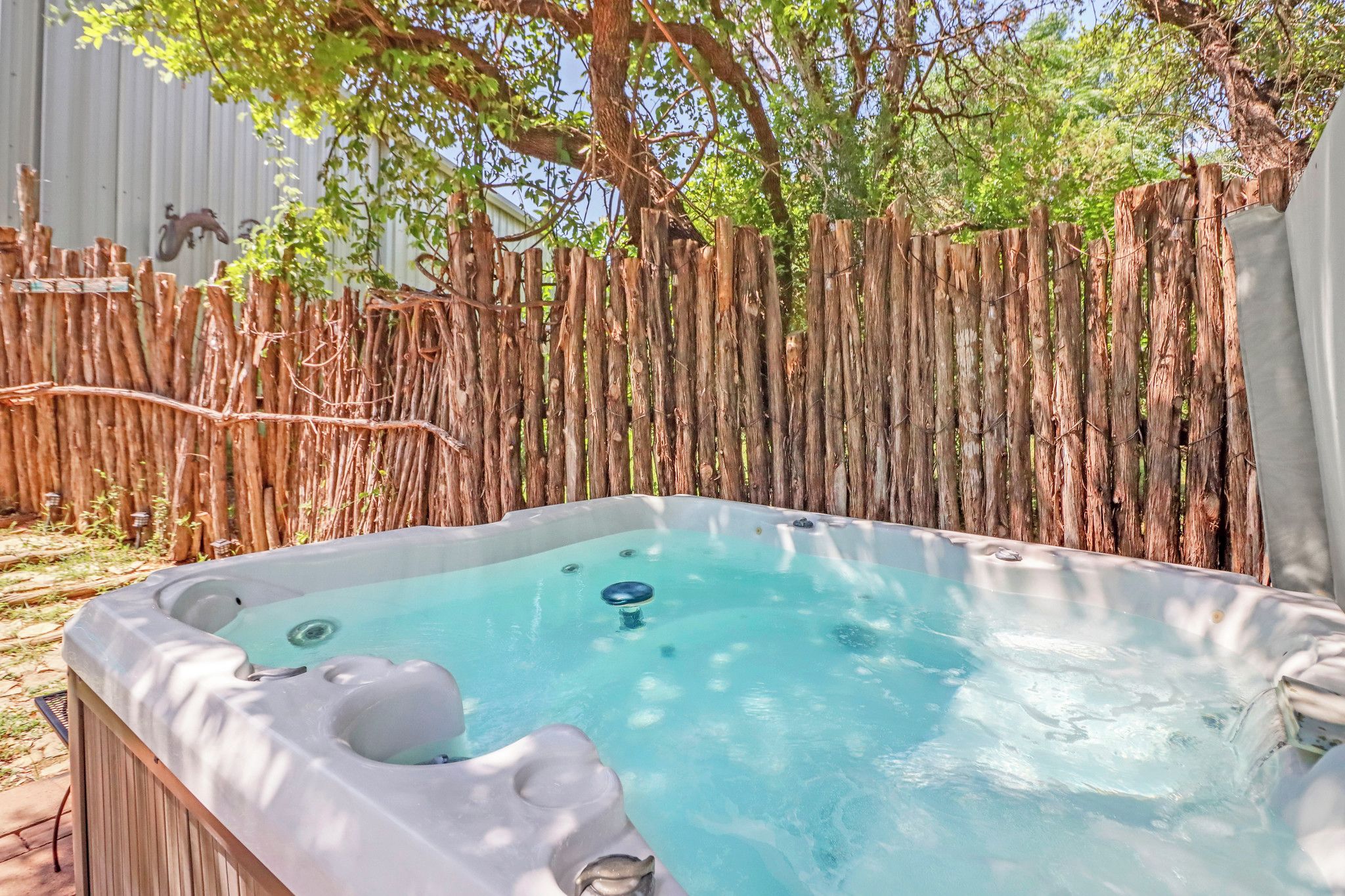 A hot tub in a backyard with a wooden fence and trees.