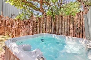 A hot tub in a backyard with a wooden fence and trees.