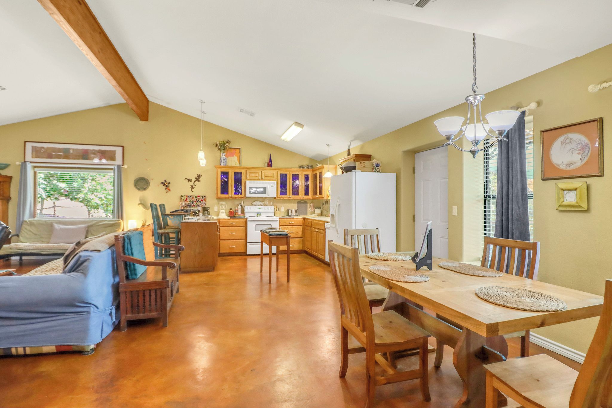 A spacious living area with a dining table, wooden chairs, a sofa, and a kitchen in the background.