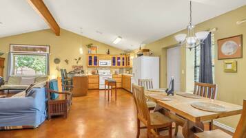 A spacious living area with a dining table, wooden chairs, a sofa, and a kitchen in the background.