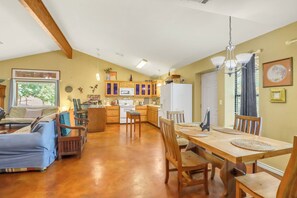 Un vaste espace de vie comprenant une table à manger, des chaises en bois, un canapé et, au fond, une cuisine.