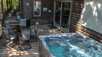 Una terraza de madera con un jacuzzi, mobiliario exterior y una zona de patio techada.
