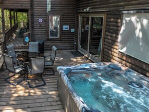 Una terraza de madera con un jacuzzi, mobiliario exterior y una zona de patio techada.