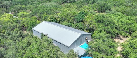 A large industrial building surrounded by dense greenery, with a swimming pool in the foreground.